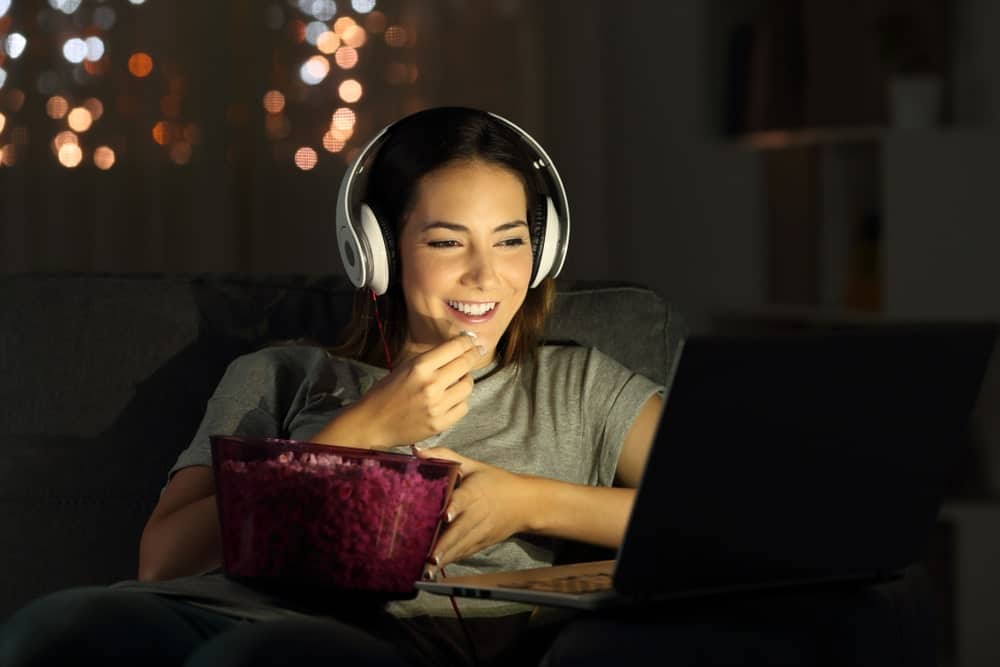 Woman watching movie at night with headphones eating popcorn